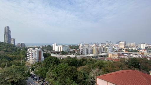Panoramic cityscape from a high viewpoint showing buildings, tree-lined streets, and distant sea view