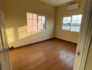 Empty bedroom with wooden flooring, open window and an air conditioner