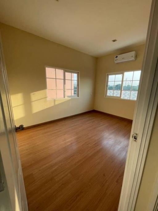 Empty bedroom with wooden flooring, open window and an air conditioner