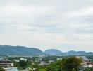 Scenic view of a town with surrounding greenery and hills under a cloudy sky