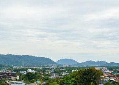 Scenic view of a town with surrounding greenery and hills under a cloudy sky