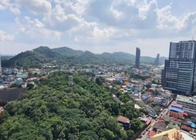 Aerial view of a cityscape with tall buildings and lush green hills under a clear sky