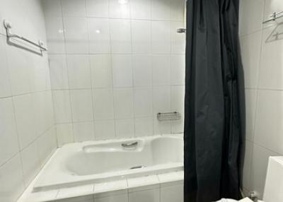 Compact white tiled bathroom with bathtub and dark curtain