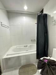 Compact white tiled bathroom with bathtub and dark curtain