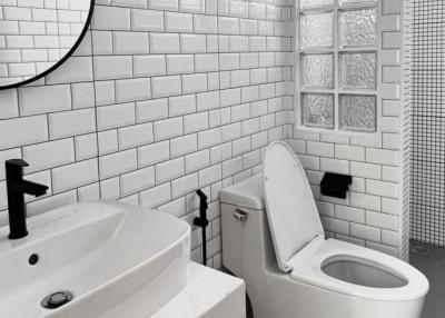 Modern white tiled bathroom with a pedestal sink, round mirror, and toilet