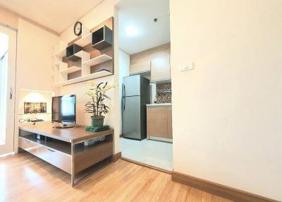 Modern living room with an open shelving unit, a desk with computer, and a full-sized refrigerator