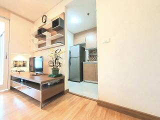 Modern living room with an open shelving unit, a desk with computer, and a full-sized refrigerator