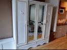 Elegant white wooden wardrobe with golden accents in a modern living space with a visible kitchenette