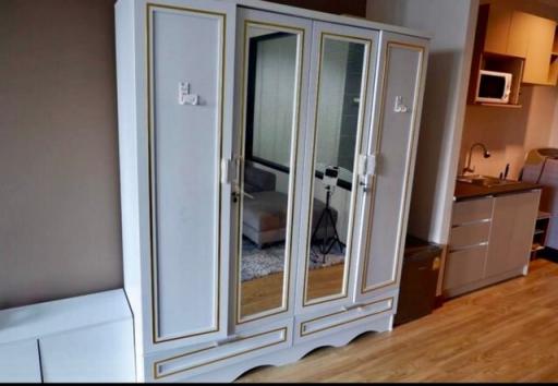 Elegant white wooden wardrobe with golden accents in a modern living space with a visible kitchenette