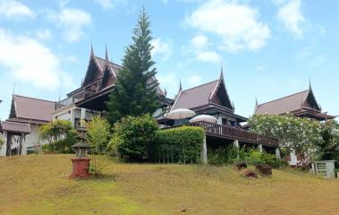 Traditional style house with multiple peaked roofs surrounded by greenery under a blue sky