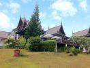 Traditional style house with multiple peaked roofs surrounded by greenery under a blue sky