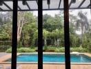 View from a house showcasing the pool and garden surrounded by lush greenery through large glass windows