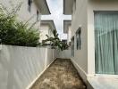 Narrow side yard of a residential house with partial greenery and potential for landscaping