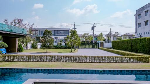 Modern suburban house with a spacious green lawn, outdoor swimming pool, and clear blue sky