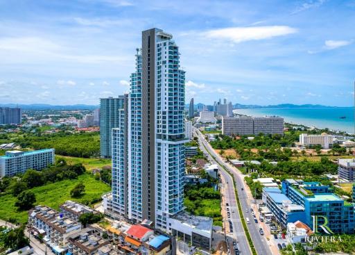 Aerial view of a modern high-rise residential building against a coastal city backdrop