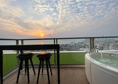 Spacious balcony with ocean view, bar stools, and a luxurious bathtub at sunset