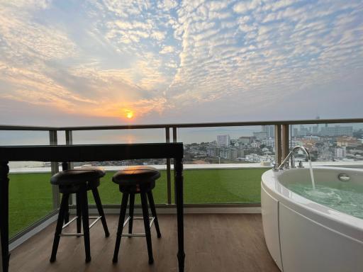 Spacious balcony with ocean view, bar stools, and a luxurious bathtub at sunset