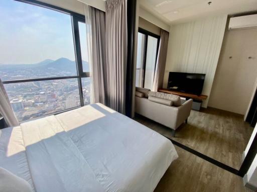Spacious bedroom with panoramic city view through floor-to-ceiling windows, featuring a large bed and a modern seating area