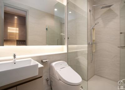 Modern bathroom with neutral tones, featuring a clear glass shower, well-lit vanity area, and ceramic fixtures