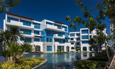 Modern apartment complex with blue and white facade surrounded by lush greenery and water feature