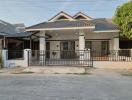 Single-story residential home with gabled roofs and front yard behind metal fence