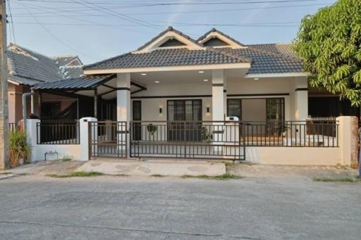 Single-story residential home with gabled roofs and front yard behind metal fence