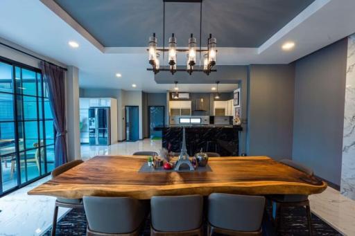 Stylish dining room with modern chandelier over a wooden table and open-plan kitchen in the background