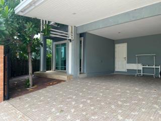 Spacious outdoor covered driveway area with a house entrance and greenery