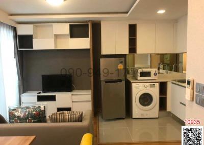 Compact living room with integrated kitchenette featuring modern appliances and cabinetry