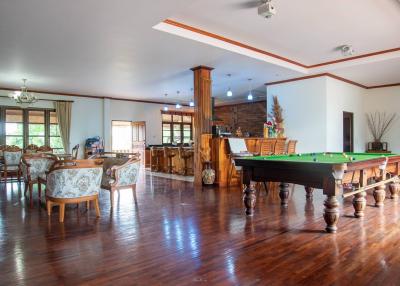 Spacious open floor plan living area with pool table, hardwood floors, and kitchen in the background