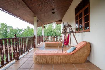 Spacious covered balcony with wicker furniture and forest view