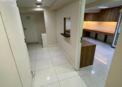 Modern hallway leading to a kitchen with wooden cabinets and tiled flooring