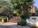 Exterior view of a residential house with a gate and lush greenery