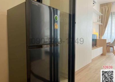 Modern apartment interior view showing a kitchen with a stainless steel refrigerator and a glimpse of the living area