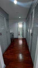 Hallway leading to a room with hardwood flooring and closed shutter doors