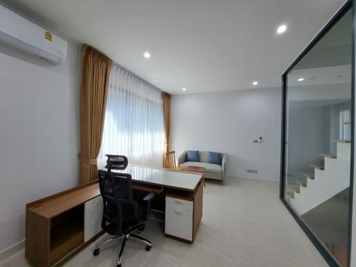 Modern home office with a desk, chair, and comfortable seating area beside a glass partition