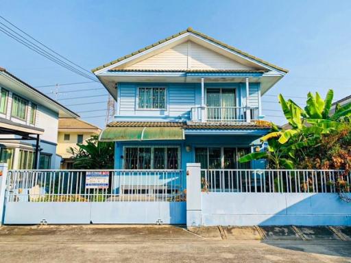 Two-story blue house with a fenced yard and tropical plants