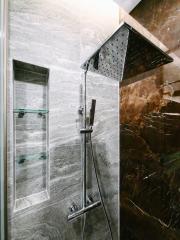 Modern sleek bathroom with large rainfall shower head and dark marble walls