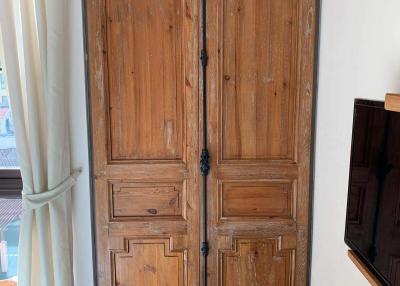 Vintage wooden double door in a living space with curtain and partial view of a television