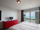 Bright bedroom with ocean view, modern red dresser, and wall-mounted television