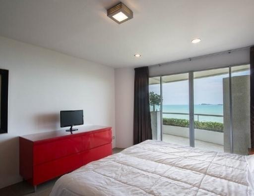 Bright bedroom with ocean view, modern red dresser, and wall-mounted television