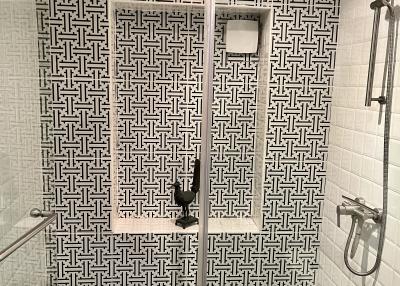 Modern bathroom with patterned tiling, glass door shower, and wall-mounted fixtures