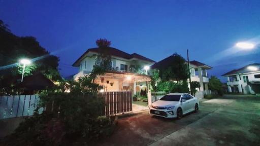 Exterior view of a two-story house during twilight with illuminated garden lights and a car parked in the driveway