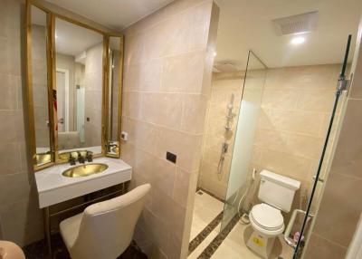 Modern bathroom interior with beige tiles, glass shower, and golden fixtures