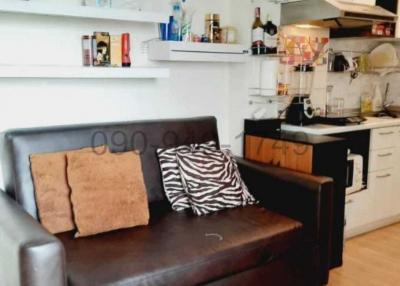 Compact living space with a brown couch, open shelving, and a kitchenette