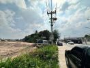 Empty lot by a roadside with utility poles and vehicles