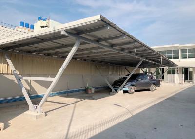 Outdoor car parking structure adjacent to a modern building with a truck parked under it