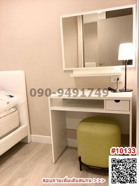 Cozy bedroom interior with modern furniture including a white bed, side table with lamp, mirror, vanity area, and comfortable ottoman