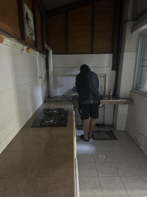 Person standing in a small, dimly lit kitchen with wooden cabinets and gas stove