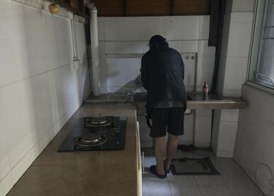 Person standing in a small, dimly lit kitchen with wooden cabinets and gas stove